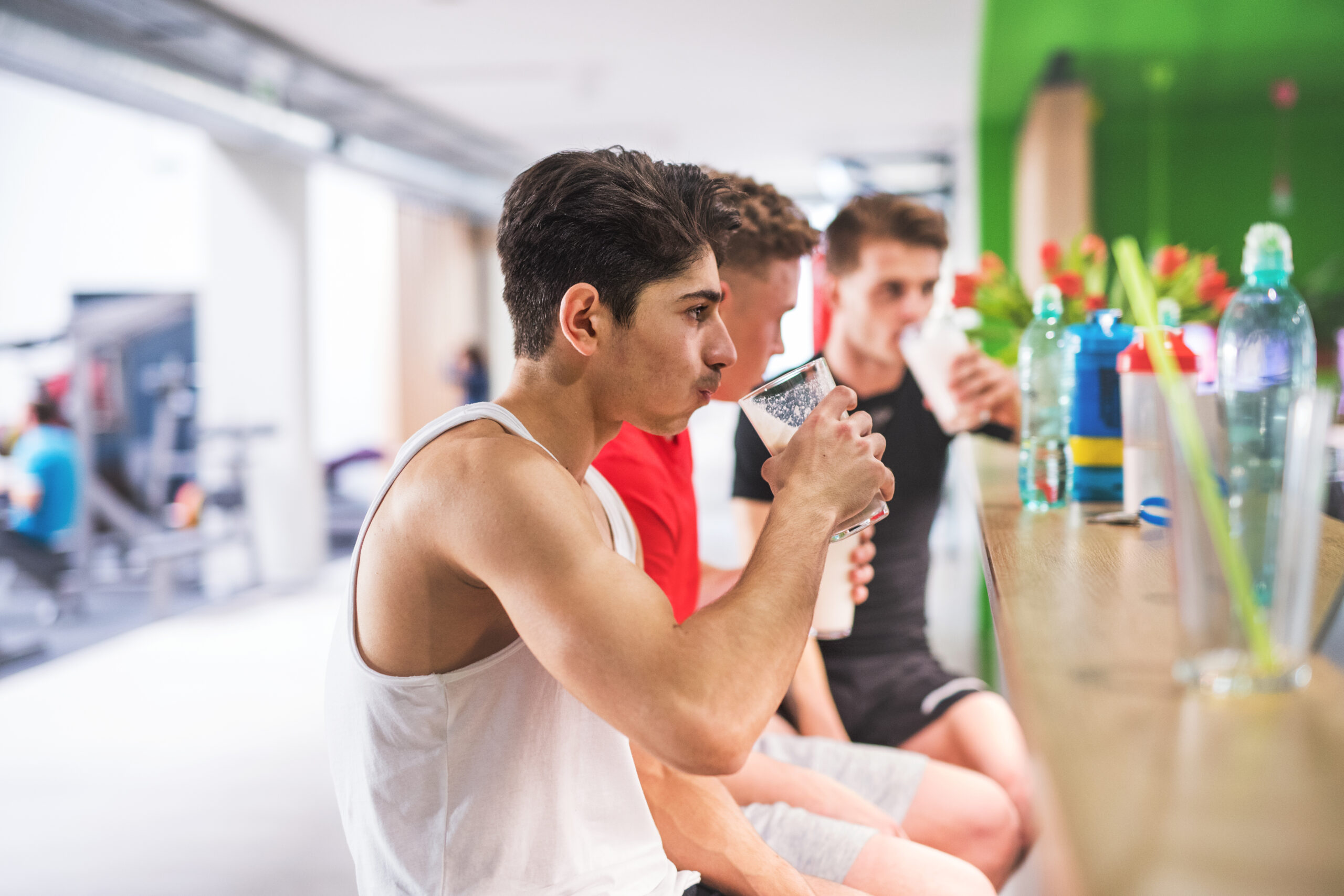 Hommes en salle de gym assis et tenant des verres de boisson protéinée.